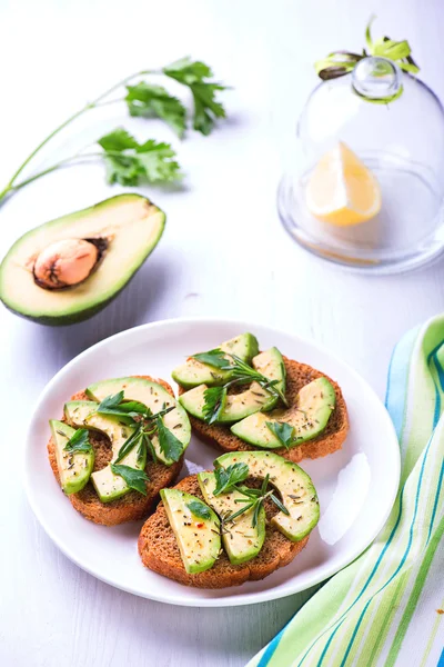 Tostadas con pan de centeno, aguacate y hierbas en plato blanco — Foto de Stock