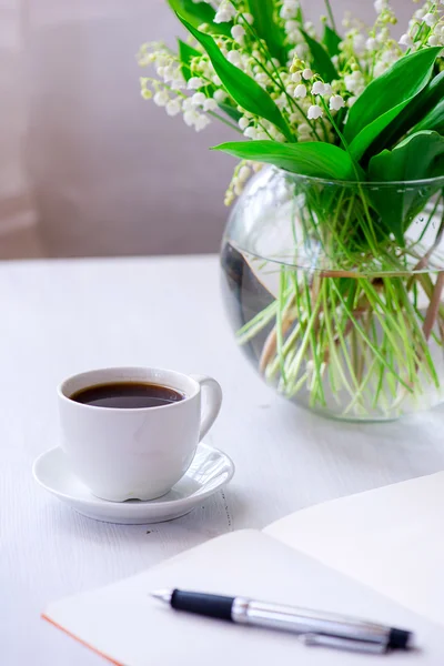 Beautiful lily of the valley with notebook and pen and cup of co — Stock Photo, Image