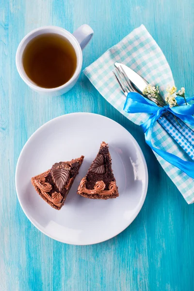 Chocolate cake with tea on a plate on blue background — Stock Photo, Image