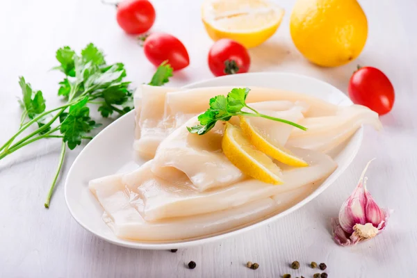 Rå bläckfisk och ingredienser på en vit platta — Stockfoto