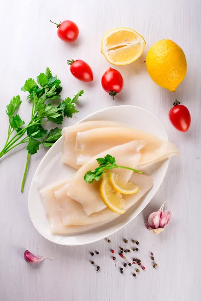 Rå bläckfisk och ingredienser på en vit platta — Stockfoto