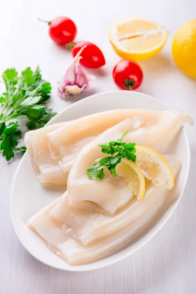 Rå bläckfisk och ingredienser på en vit platta — Stockfoto