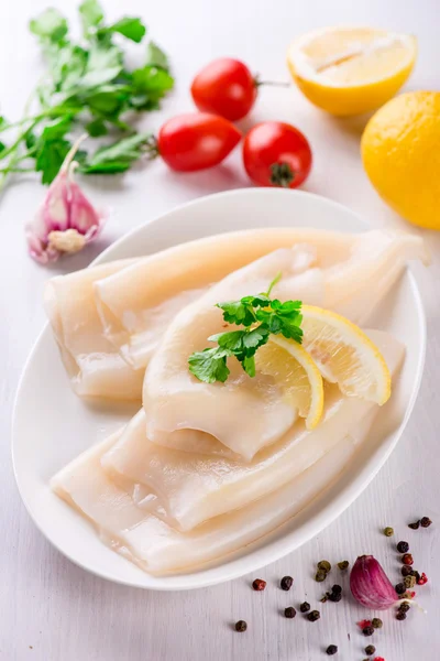 Rå bläckfisk och ingredienser på en vit platta — Stockfoto