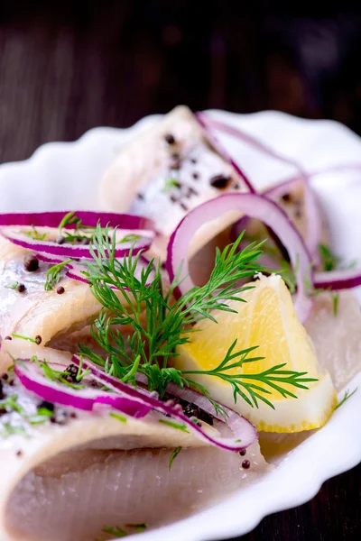 Herring with pepper, herbs, salt and lemon on white ceramic plat — Stock Photo, Image