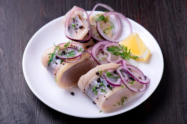 Biber, otlar, tuz ve limon üzerinde beyaz seramik plat ile ringa balığı