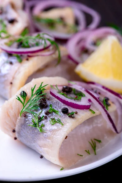 Biber, otlar, tuz ve limon üzerinde beyaz seramik plat ile ringa balığı