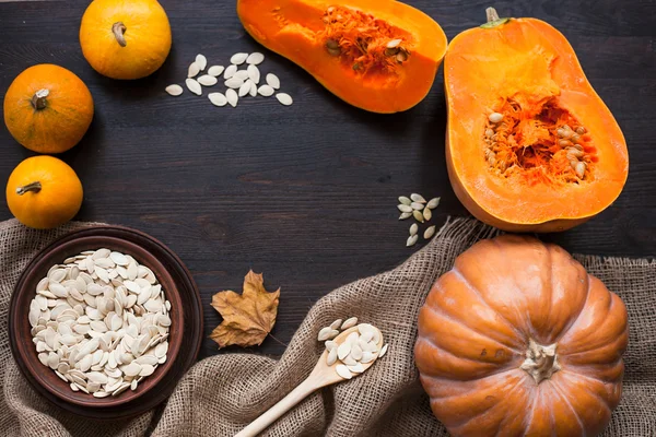 Pumpkins and a bowl with toasted pumpkin seeds, wooden spoon — Stock Photo, Image