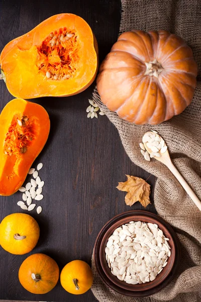 Pumpkins and a bowl with toasted pumpkin seeds, wooden spoon — Stock Photo, Image