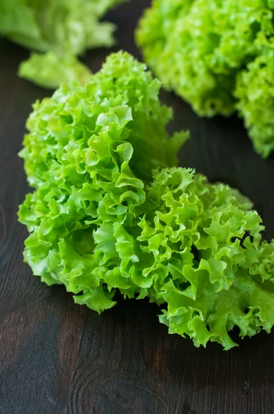 Fresh green salad leaves (lettuce) on black wooden table — Stock Photo, Image