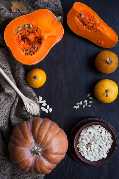 Pumpkins and a bowl with toasted pumpkin seeds, wooden spoon — Stock Photo, Image