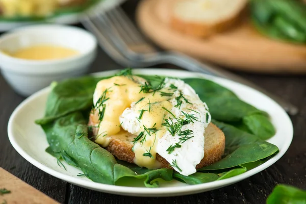 Poached egg on a piece of bread with spinach on the wooden table — Stock Photo, Image