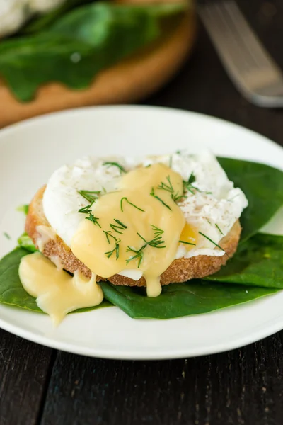Huevo escalfado en un pedazo de pan con espinacas en la mesa de madera — Foto de Stock
