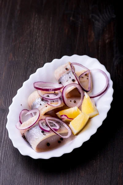 Aringa con pepe, erbe aromatiche, sale e limone su un piatto di ceramica bianca — Foto Stock
