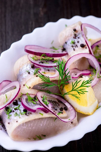 Herring with pepper, herbs, salt and lemon on white ceramic plat — Stock Photo, Image