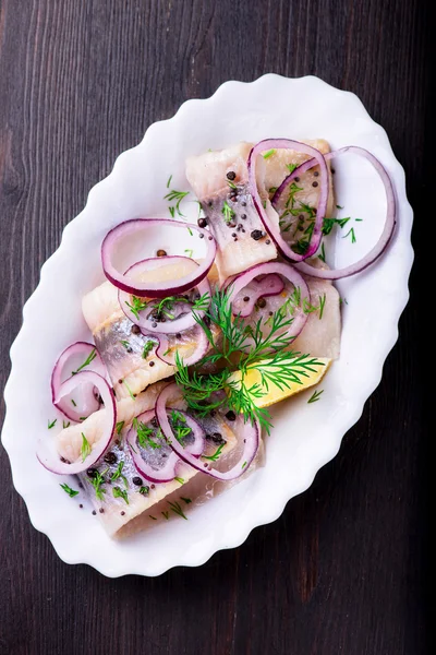 Aringa con pepe, erbe aromatiche, sale e limone su un piatto di ceramica bianca — Foto Stock