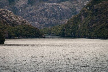 Sarmiento Kanalı, Şili - 11 Aralık 2008: Amalia Buzulu ve Fiyort. Yan silah, ışığın suyla oynadığı geniş kanala girer. Dağların engebeli koyu kayalıkları, su kenarında yeşil yapraklar..