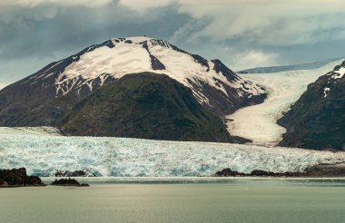 Sarmiento Kanalı, Şili - 11 Aralık 2008: Kara kayalar arasındaki fiyort suyunda eriyen Amalia Buzulu 'na yakından bakın. Mavimsi renk ve yeşilimsi su. Yukarıdaki kalın gri bulut.