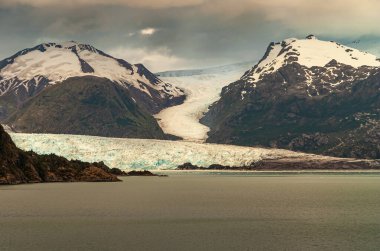 Sarmiento Kanalı, Şili - 11 Aralık 2008: Amalia Buzulu 'nun fiyorda inişi. 2 büyük, siyah kar kaplı kaya ve bulutlu hava..