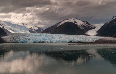 Sarmiento Kanalı, Şili - 11 Aralık 2008: Amalia Buzulunun erimesi ağır kahverengi bulutlar altında karanlık suya yansıdı. Siyah dağ kayaları arasında buz akıntıları.