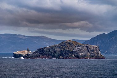 Horn Burnu, Wollaston Adaları, Şili - 14 Aralık 2008: Bulutların altındaki mavi sulardaki kuşlar tarafından kirletilmiş kaya adalarına yakın çekim. Arkaplan olarak büyük ada.
