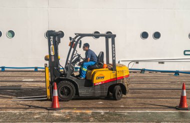 Montevideo, Uruguay - 18 Aralık 2008: Limanda siyah-sarı DPM forklift kullanan erkek işçinin kapatılması. Arka plan olarak büyük geminin beyaz tarafı. Kırmızı külahlar öne..