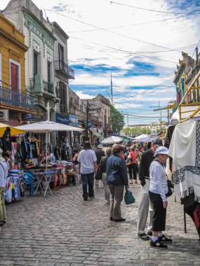 Buenos Aires, Arjantin 19 Aralık 2008, La Boca Mahallesi. Sıradan mağazaların ve mavi bulutların altında evlerin önüne kurulmuş dandik kabinleri olan bir sokak pazarı. Bir sürü müşteri var..