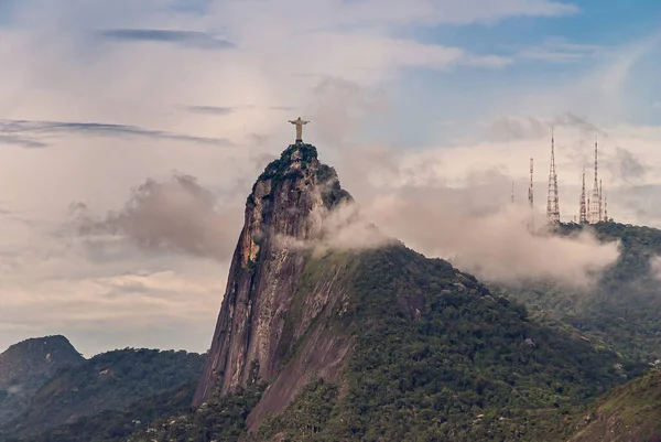巴西里约热内卢 2008年12月22日 基督的救世主雕像在绿色森林的山顶上 灰色的云彩下有陡峭的悬崖 其他山上的一些高耸的天线 — 图库照片