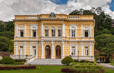 Petropolis, Brezilya - 23 Aralık 2008: Palacio Rio Negri 'nin beyaz çerçeveli sarı ön cephe önü, veya mavi bulutların altındaki yeşil parktaki siyah nehir sarayı
