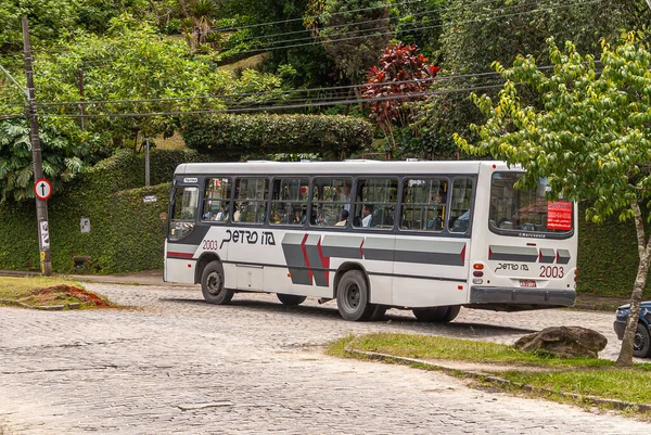 Petropolis, Brezilya - 23 Aralık 2008: Beyaz toplu taşıma otobüsü yeşil yapraklara karşı taş kaldırımda.