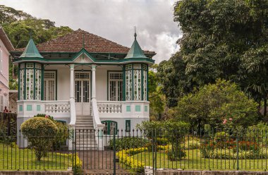 Petropolis, Brezilya - 23 Aralık 2008: Küçük yeşil kuleleri ve kırmızı çiçekli bahçesinde kırmızı çatısı olan tarihi eski beyaz villa. Gri ağaçlar ve gri bulutlar.