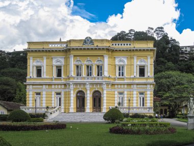 Petropolis, Brezilya - 23 Aralık 2008: Palacio Rio Negri 'nin beyaz çerçeveli sarı ön cephe önü, veya mavi bulutların altındaki yeşil parktaki siyah nehir sarayı