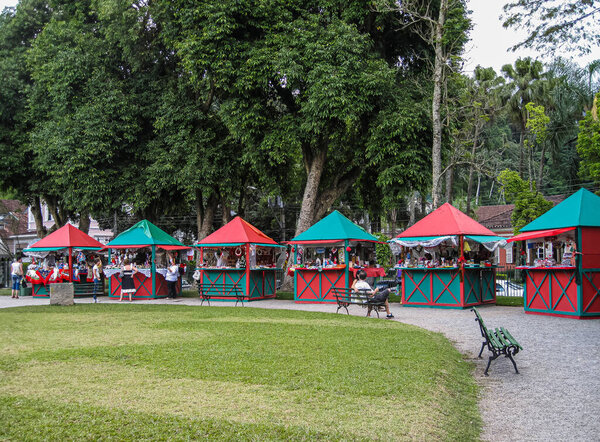 Petropolis, Brazil - December 23, 2008: Christmas in green park: Row of green-red market booths with vendors and customers in front of green trees.