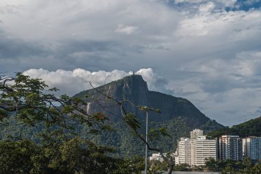 Rio de Janeiro, Brezilya - 23 Aralık 2008: Yeşil Lagoa Rodrigo de Freitas üzerinden batıya doğru bakan Kurtarıcı İsa heykeli, dağın tepesinde, ağır mavi bulutların altında. Apartman kemeri.