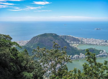 Rio de Janeiro, Brezilya - 24 Aralık 2008: Bairro Peixito 'nun yeşil yeşil ormanlı tepesinin havadan görünüşü ve çevresindeki mahalleler ve yeşil göl. açık mavi bulutlar altında adaları olan mavi okyanus.