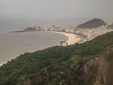Rio de Janeiro, Brezilya - 25 Aralık 2008: Noel günü. Gökyüzü ve okyanus suyu aynı gri renge dönüştüğünde Copacabana sahilindeki hava manzarası. Önde, Sugarloaf Dağı 'nın yeşil yaprakları.