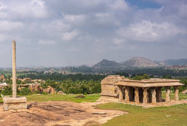 Hampi, Karnataka, Hindistan - 4 Kasım 2013: Sunset Hill namı diğer Hemakatu. Tepedeki tapınağın yıkıntıları ve sütunları zengin tarım arazilerinin önünde, ufuktaki kayalık tepeler mavi bulutların altında.
