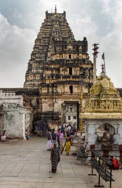 Hampi, Karnataka, Hindistan - 4 Kasım 2013: Virupaksha Tapınağı Kompleksi. Yarı kapının önündeki renkli elbiseli insanlar kısa gopuram ve uzun doğu gopuram ile bulutların altında..