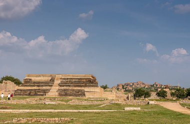 Hampi, Karnataka, Hindistan - 4 Kasım 2013: Mahanavami Dibba veya Dussehra Platformu Zafer Sarayı 'ndan geriye kalanlar. Mavi bulutların altında kahverengi taşlar. Önünde yeşil ot olan daha geniş bir alan..