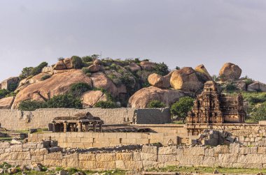 Hampi, Karnataka, Hindistan - 4 Kasım 2013: Hazare Rama Tapınağı yıkıcı bej duvarların arkasında. Açık mavi gökyüzü ve arkadaki büyük kahverengi kaya tepeleri.
