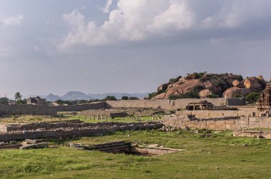 Hampi, Karnataka, Hindistan - 4 Kasım 2013: Kraliyet Koruması. Kuzey kısmı, artık bulutların altında harabelerle dolu yeşil bir arazi. Hazara Rama Tapınağı kulesi arkada..