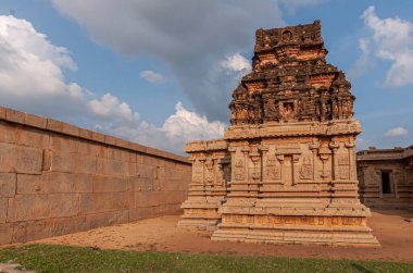 Hampi, Karnataka, Hindistan - 4 Kasım 2013: Hazara Rama Tapınağı. Koyu kahverengi Vimanam kulesiyle daha küçük dekore edilmiş bina gün batımında mavi bulutların altında, dış duvarın yakınında izole edilmiş..