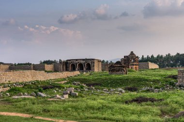 Hampi, Karnataka, Hindistan - 4 Kasım 2013: Açık mavi günbatımı bulutları altında 3 kapılı cami harabeleri ve Müslüman soyluların kamarasındaki diğer binaların manzarası. Çimenler öne..