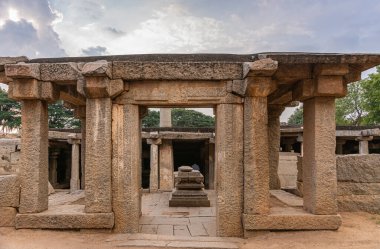 Hampi, Karnataka, Hindistan - 4 Kasım 2013: Prasanna Virupaksha yeraltı Shiva Tapınağı. Kahverengi taş kalıntıları günbatımı bulutlarının altında, daha düşük bir tapınağın önünde yatıyor..