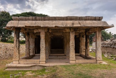 Hampi, Karnataka, Hindistan - 4 Kasım 2013: Prasanna Virupaksha yeraltı Shiva Tapınağı. Kahverengi taş Mandapam Salonu Akşam gökyüzünün ve çevrenin altında yeşil yaprakların altında.