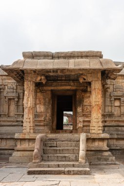 Hampi, Karnataka, Hindistan - 5 Kasım 2013: Sri Krishna tapınağı yıkıldı. Kahverengi taş basamaklı balyalarla gümüş gökyüzünün altındaki gizli mabede giriliyor. Yeşil yapraklara bak..