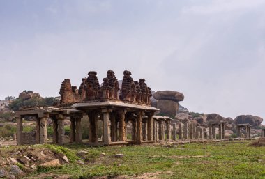 Hampi, Karnataka, Hindistan - 5 Kasım 2013: Sri Krishna tankı harabe halinde. Kahverengi taş tapınak enkazı, açık mavi gökyüzünün altındaki yıkıcı galerinin sonunda yontulmuş sütunlar. Kayalar arkada, çimenler önde..