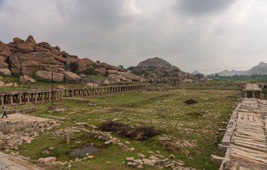 Hampi, Karnataka, Hindistan - 5 Kasım 2013: Sri Krishna tankı harabe halinde. Bir sürü gri taşı olan yeşil bir uçak ufka kadar uzanıyor. Yıkım galerisi ve yamaçlarda kayalar.