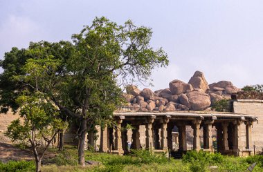 Hampi, Karnataka, Hindistan - 5 Kasım 2013: Badavilinga Tapınağı doğal yeşil bitki örtüsü ve büyük kahverengi kayalarla çevrili. Küçük harabe kahverengi taş tapınak binası.