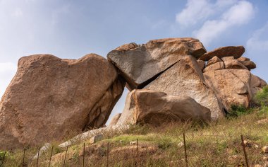 Hampi, Karnataka, Hindistan - 5 Kasım 2013: Kahverengi taş kayalardan oluşan kardeş taşlar grubu. Mavi bulutlu ve yeşil yapraklı.