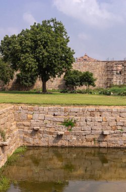 Hampi, Karnataka, Hindistan - 5 Kasım 2013: Zanana Enclosure. Queens havuzu ya da tankın köşesinde yeşil yeşillik ve koruma duvarı açık mavi bulutların altında. İskeleler arkada..